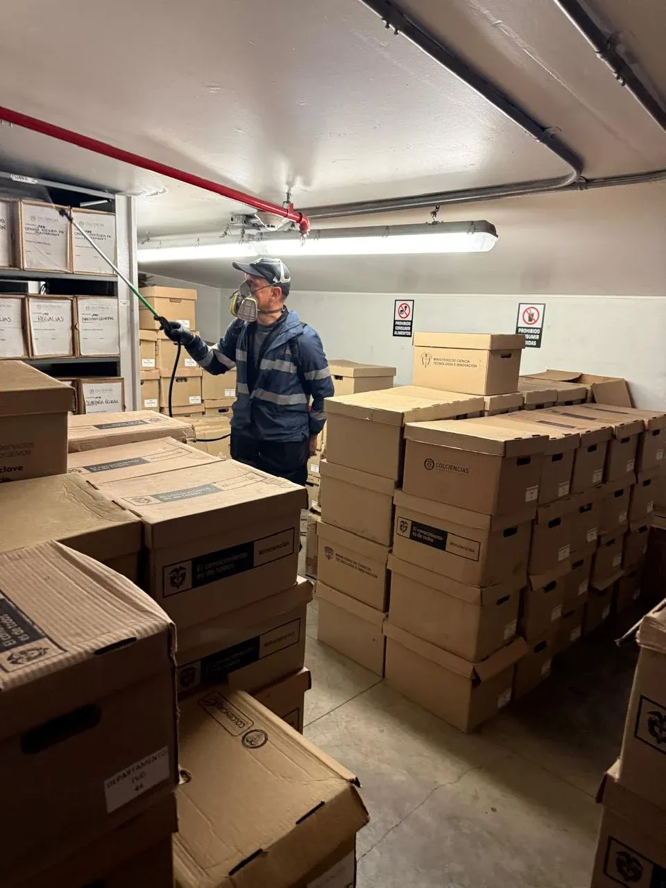 Técnico aplicando control de plagas en una bodega con cajas de archivo en Bogotá
