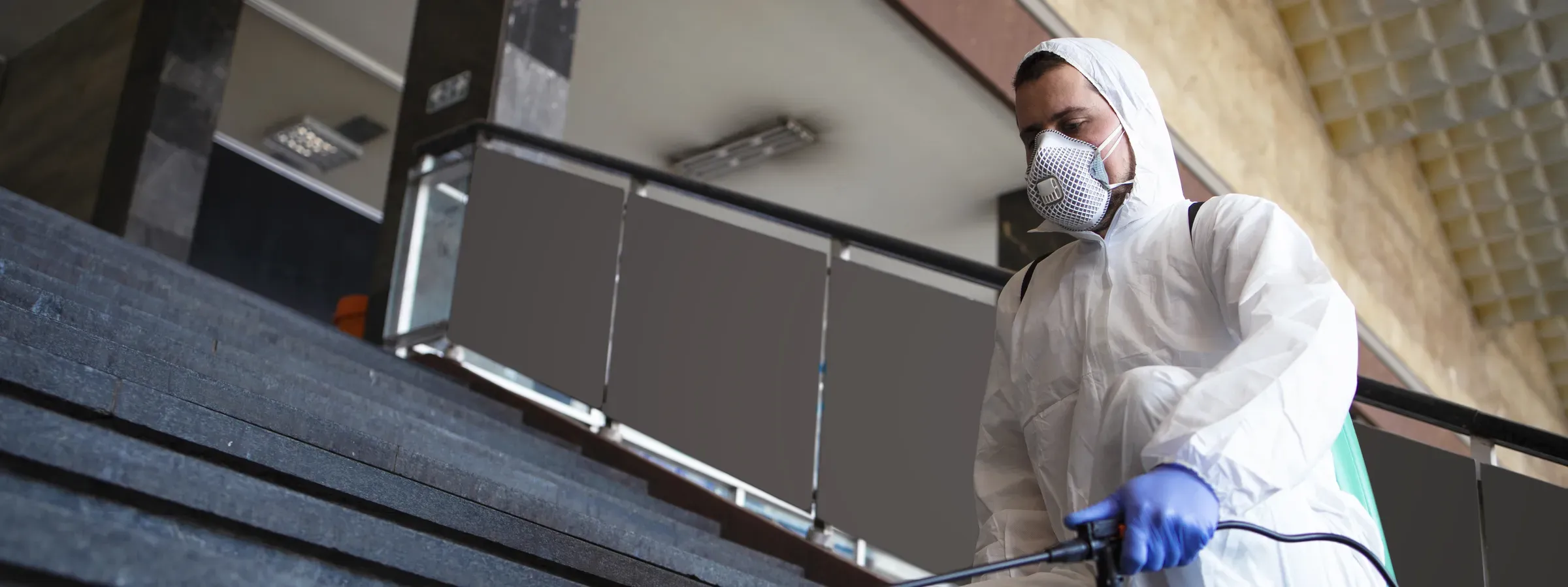Técnico con overol blanco y tapabocas fumigando las escaleras de entrada de un edificio de oficinas en Bogotá
