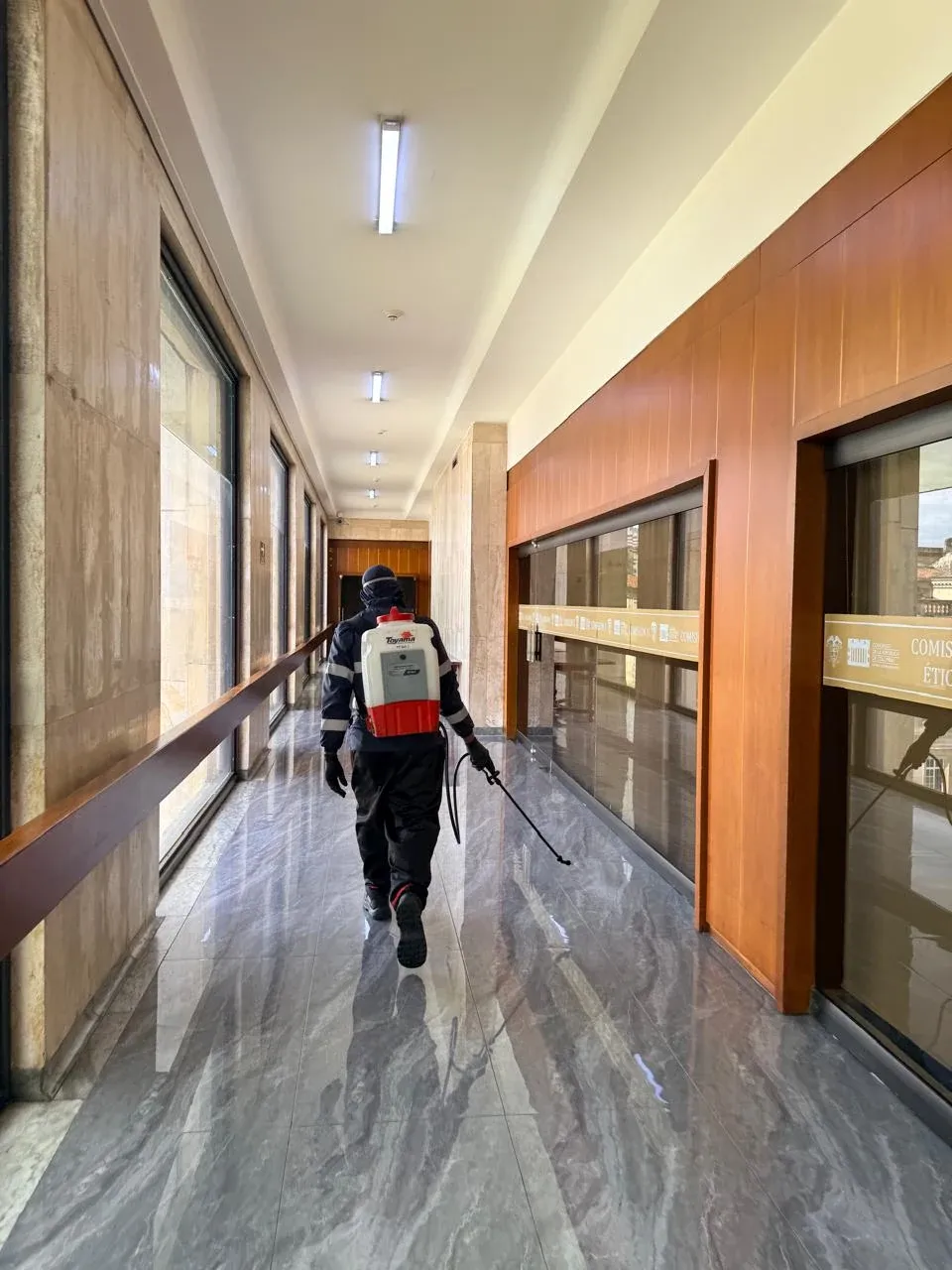 Técnico con fumigadora de espalda recorriendo el pasillo de un edificio de oficinas en Bogotá