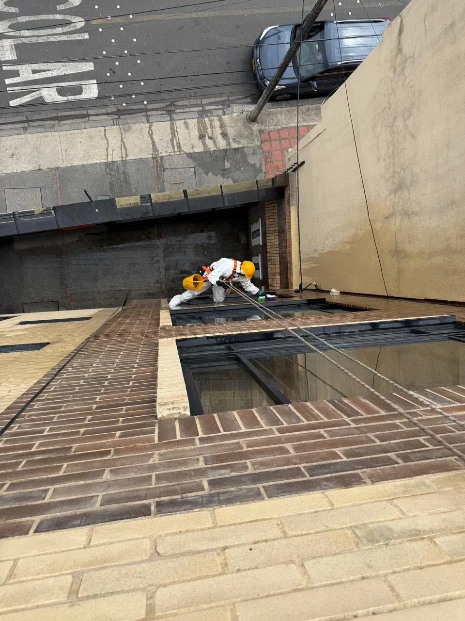 Técnico con arnés lavando una fachada de ladrillo en trabajo en alturas, visto desde la cubierta