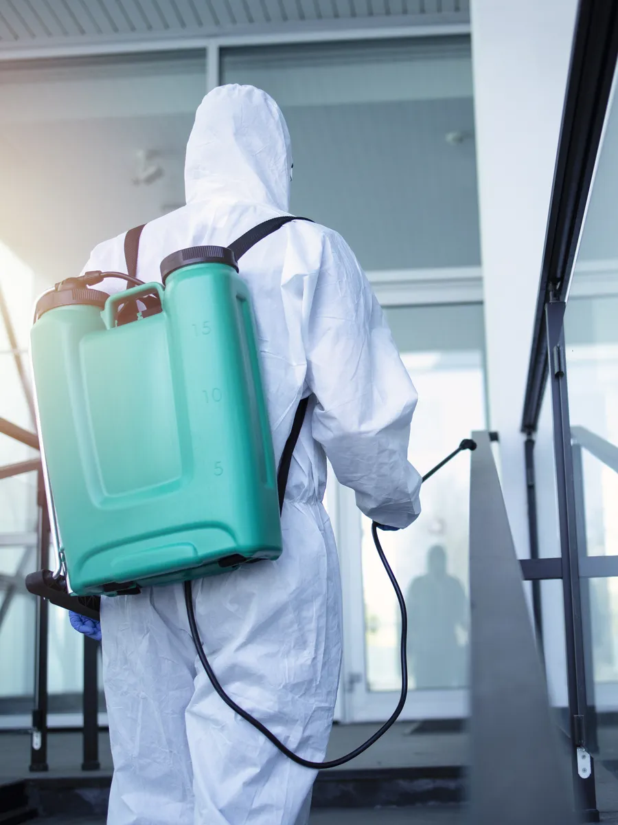 Técnico con overol blanco y tanque de fumigación a la espalda subiendo la rampa de entrada de un edificio en Bogotá